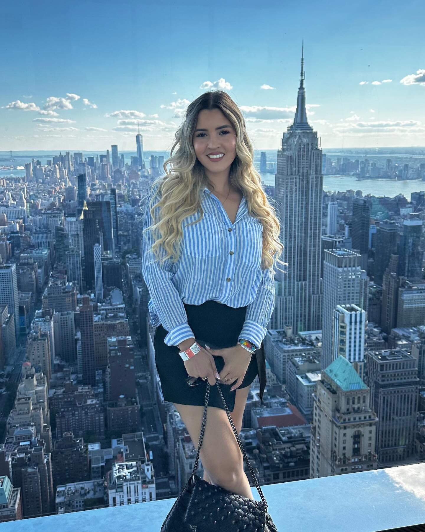 Luisa smiling in a blue striped shirt and black skirt with the New York skyline behind her
