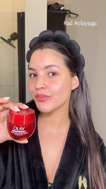 Luisa holding an Olay skincare jar while wearing a skincare headband